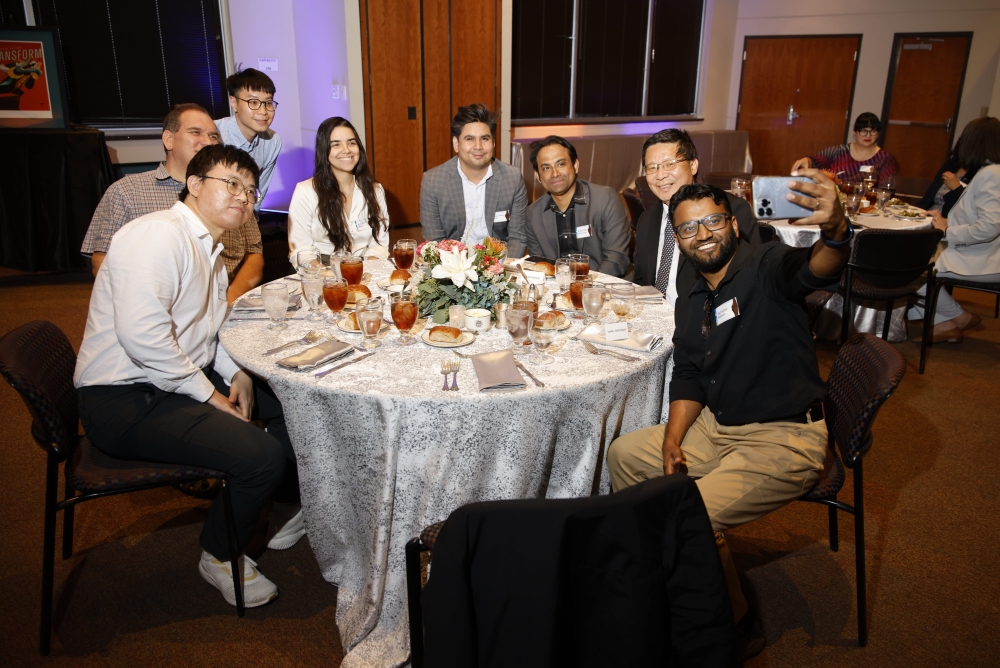 A group of attendees gathers around a banquet table for a selfie.